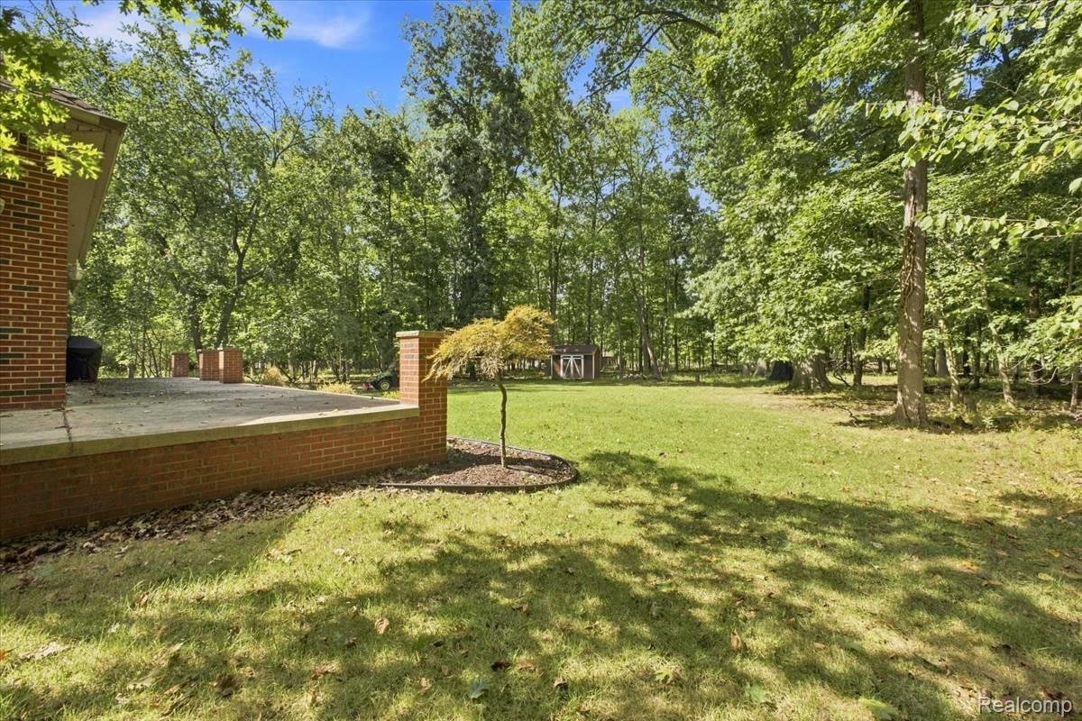 8610 Ferry Road Grosse Ile, MI 48138 - Photo 4 of 55 Expansive backyard featuring a manicured lawn, mature trees, and a brick patio with stone capping