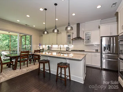 a kitchen with stainless steel appliances granite countertop a stove a refrigerator a kitchen island a dining table and chairs with wooden floor