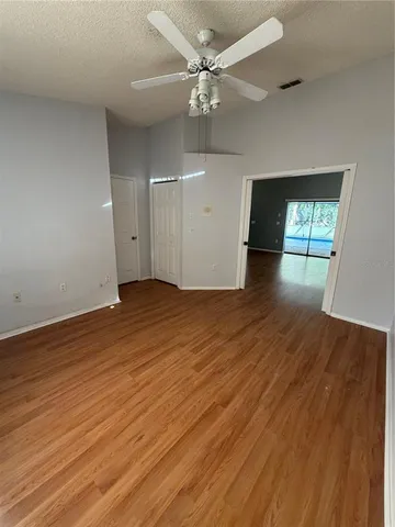 an empty room with wooden floor chandelier fan and windows