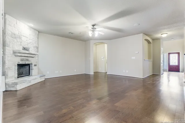 an empty room with wooden floor fireplace and ceiling fan
