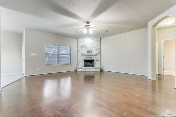 an empty room with wooden floor chandelier fan and windows