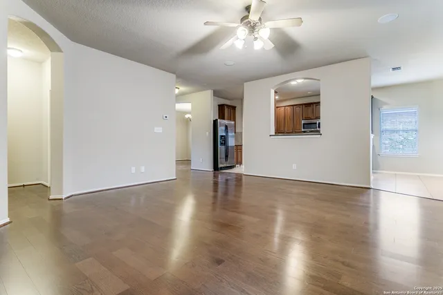 a view of an empty room with wooden floor and a ceiling fan