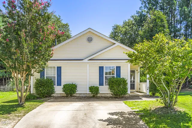 a view of a white house next to a yard with big trees