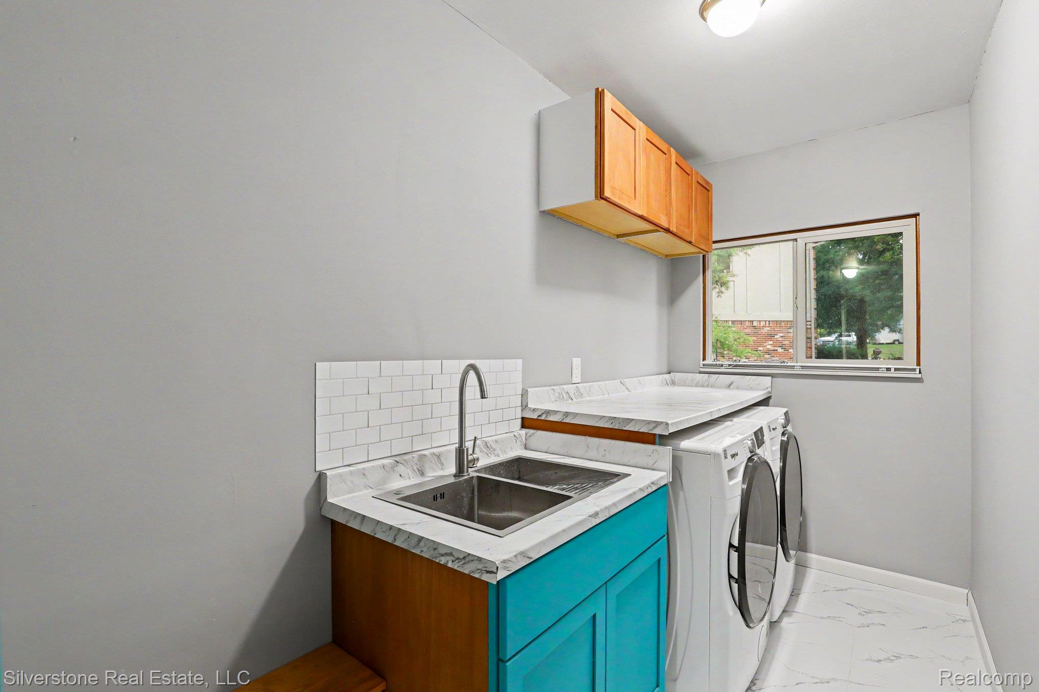 869 Timberline Drive Rochester, MI 48309 - Photo 21 of 29 Laundry area with a stainless-steel utility sink, white subway tile backsplash, and light wood-finish cabinetry