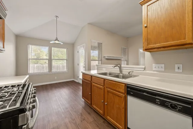 a kitchen with stainless steel appliances a sink dishwasher a stove and white cabinets with wooden floor