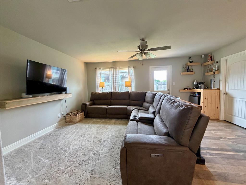 619 Mansfield Road Cleburne, TX 76031 - Photo 14 of 19 Living area featuring a ceiling fan, light gray wall paint, and a built-in wooden bar with floating shelves
