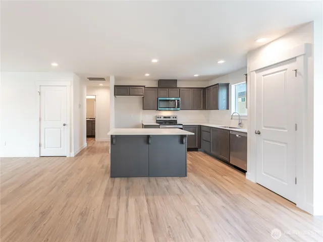 a large kitchen with stainless steel appliances kitchen island granite countertop a stove a sink dishwasher and a refrigerator with wooden floor