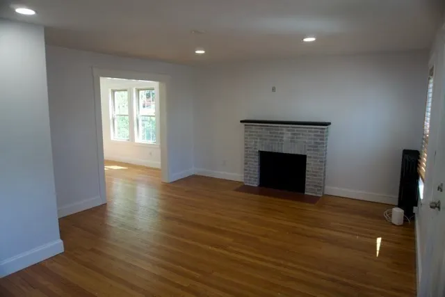 a view of an empty room with wooden floor fireplace and a window