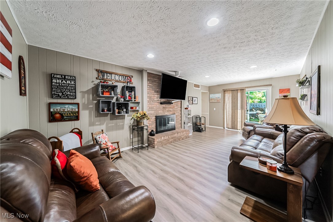 10794 Waterfall Road Strongsville, OH 44149 - Photo 16 of 37 Living room with wooden walls, wood finished floors, a brick fireplace, a textured ceiling, and recessed lighting