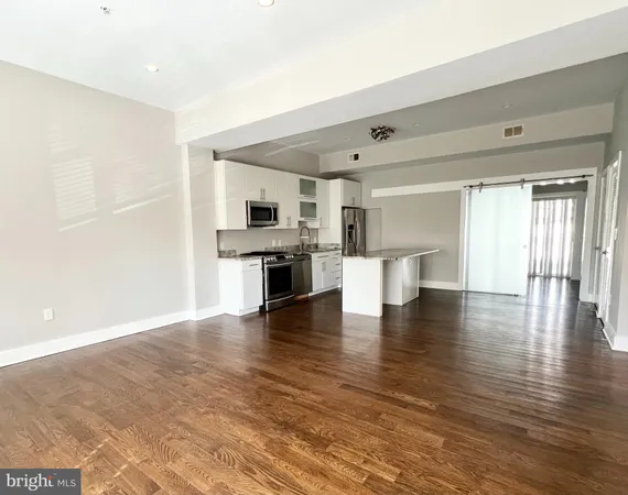 a view of an empty room with kitchen and window