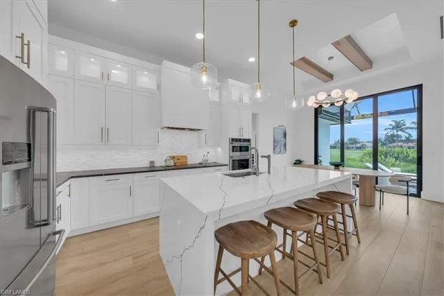 an open kitchen with granite countertop a stove a sink a refrigerator and white cabinets with wooden floor