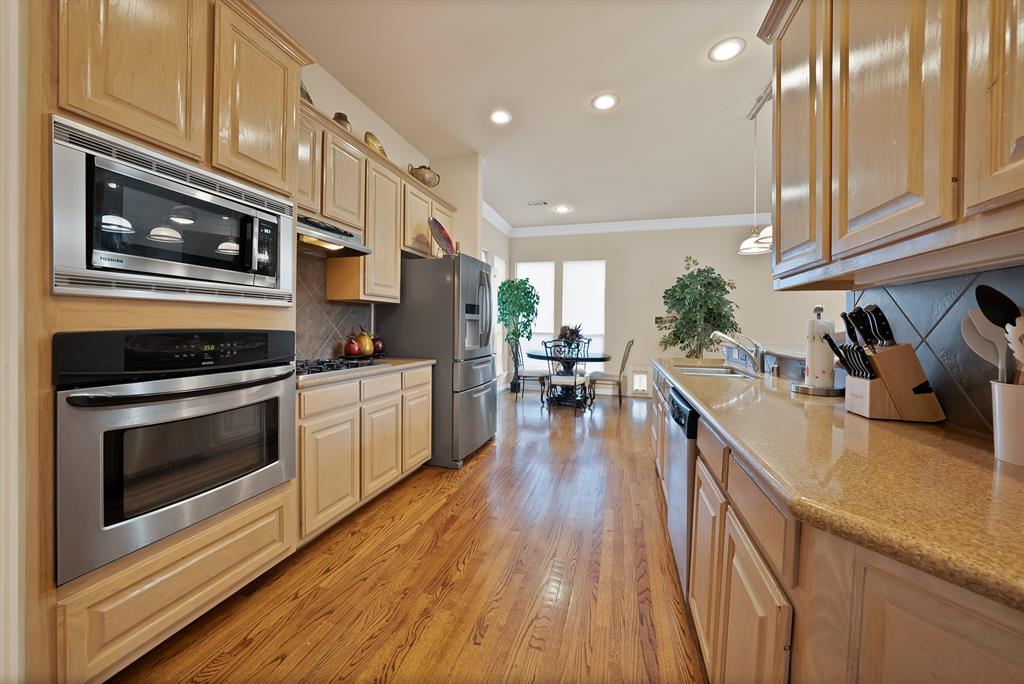 1014 Ricci Court Irving, TX 75062 - Photo 9 of 30 Kitchen featuring backsplash, appliances with stainless steel finishes, light wood-style flooring, pendant lighting, and crown molding