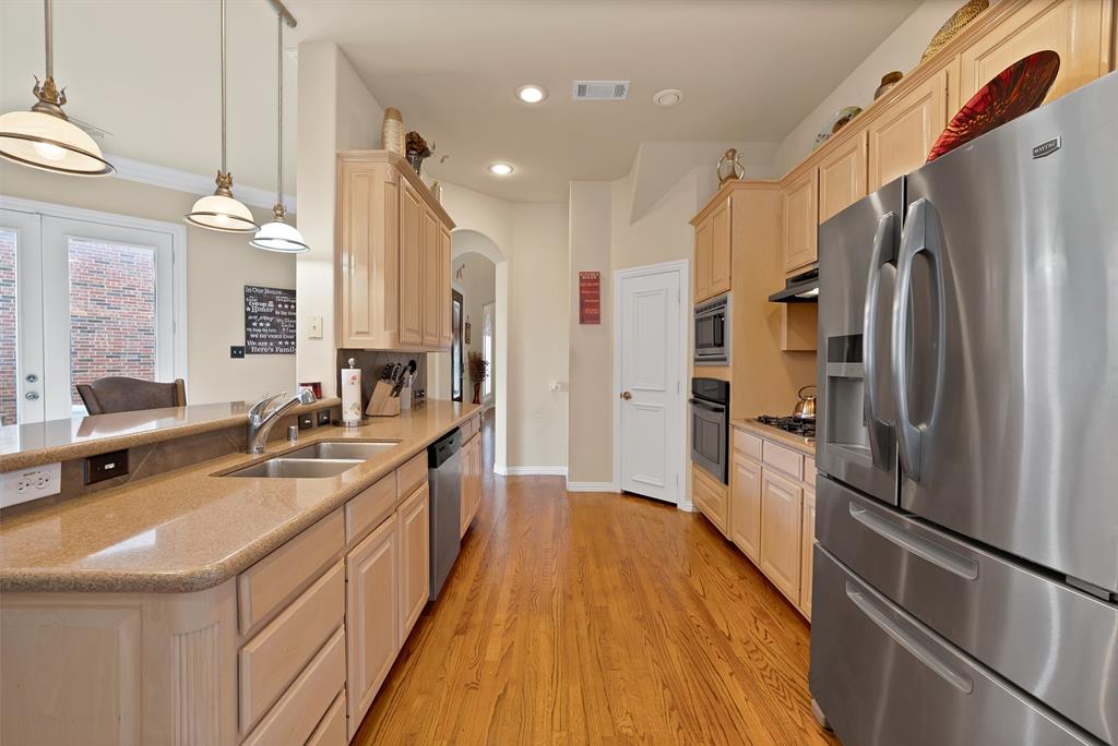 1014 Ricci Court Irving, TX 75062 - Photo 10 of 30 Kitchen with stainless steel appliances, arched walkways, hanging light fixtures, light wood finished floors, and light stone countertops