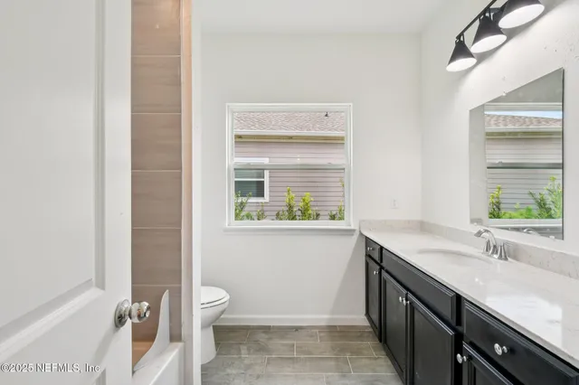 a bathroom with a granite countertop sink a toilet and a window