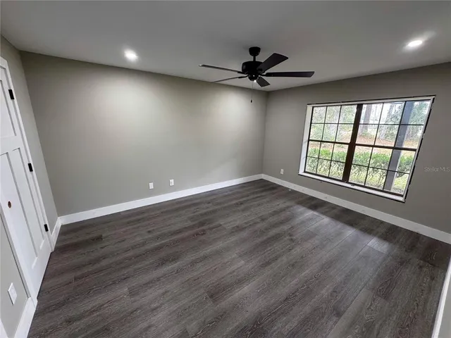 an empty room with wooden floor fan and windows