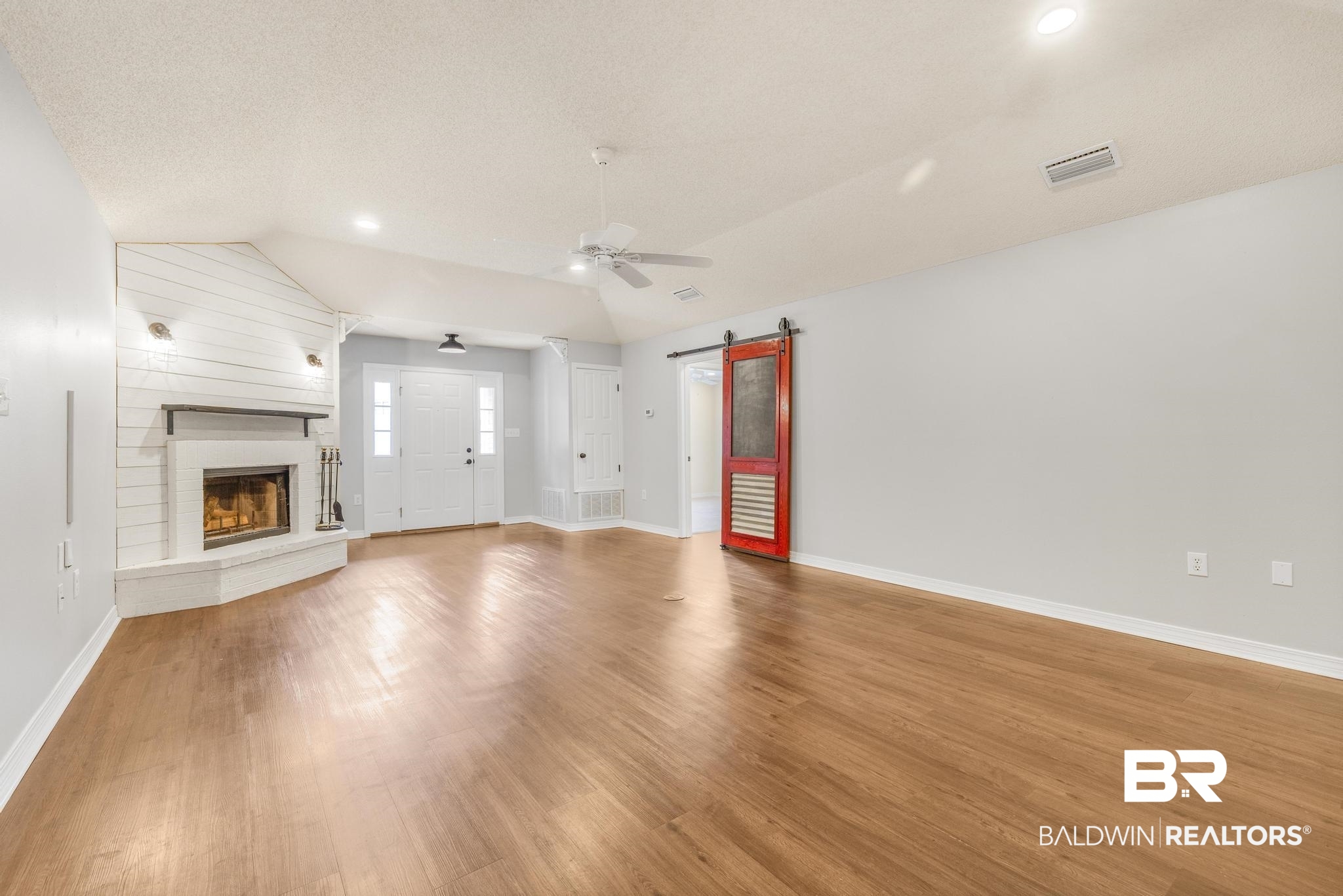 140 Hope Drive Daphne, AL 36526 - Photo 3 of 54 Unfurnished living room featuring lofted ceiling, a barn door, wood finished floors, a large fireplace, and a ceiling fan