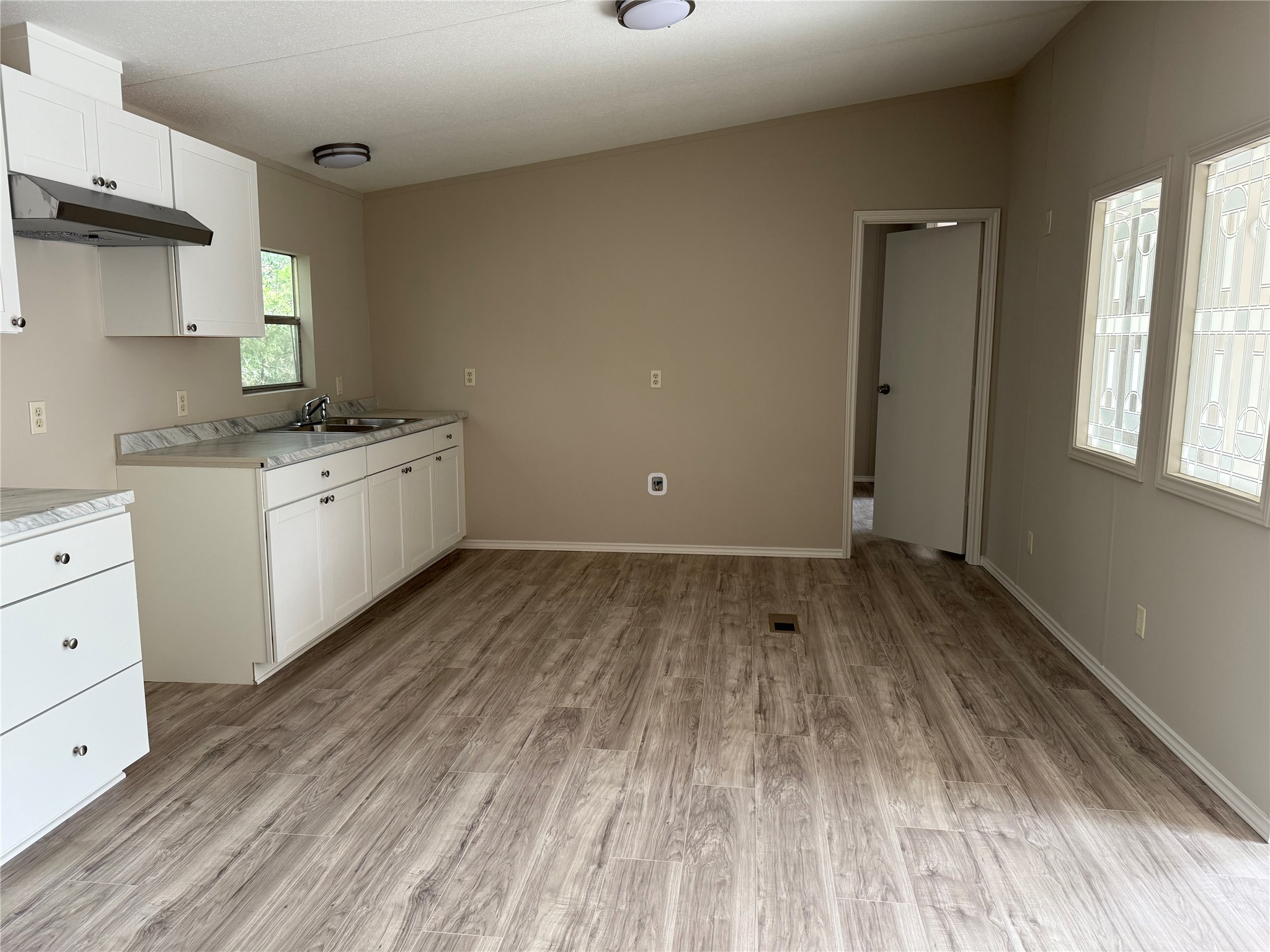 20701 Liveoak Lane Manor, TX 78653 - Photo 22 of 31 Kitchen with white cabinets, light countertops, under cabinet range hood, light wood-style flooring, and vaulted ceiling