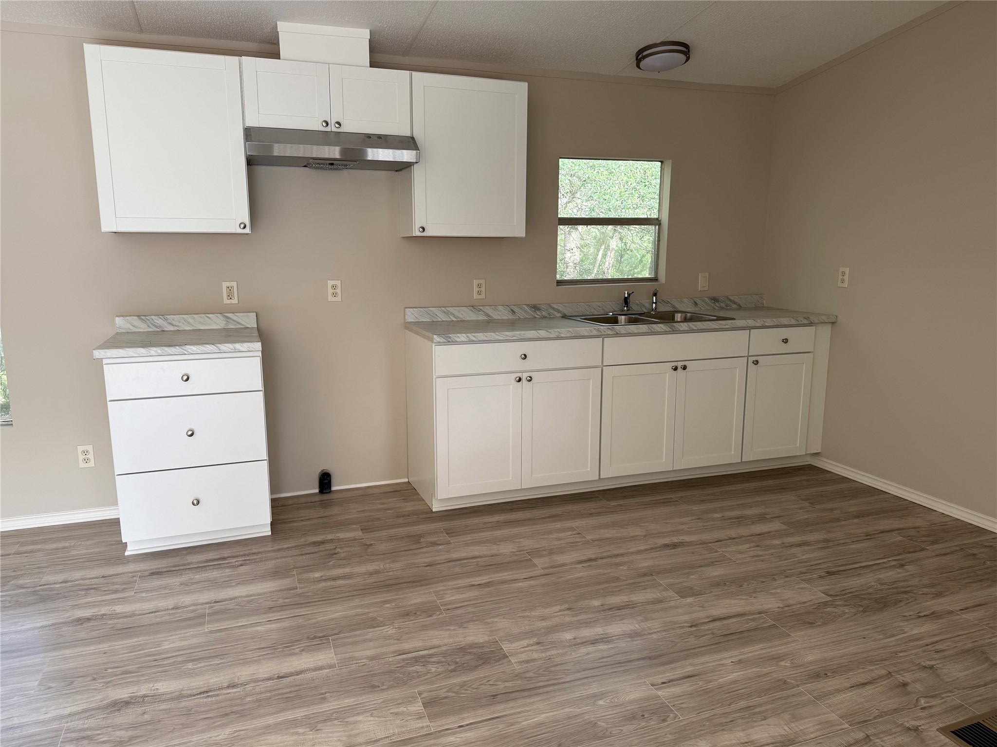 20701 Liveoak Lane Manor, TX 78653 - Photo 23 of 31 Kitchen with white cabinets, light countertops, light wood-type flooring, under cabinet range hood, and ornamental molding