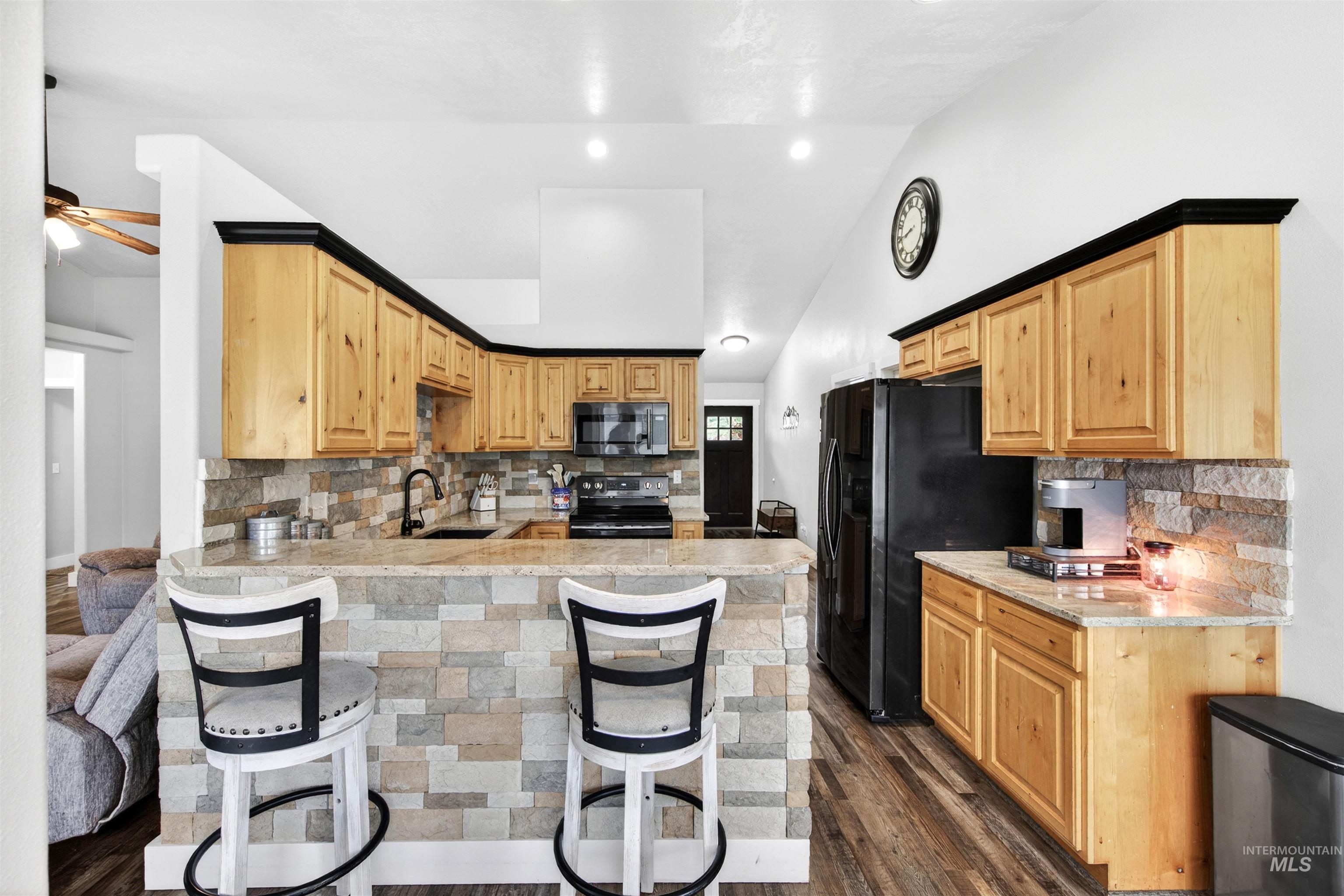 4 Round Up Circle Boise, ID 83716 - Photo 11 of 47 Open-concept kitchen featuring wood cabinetry with black trim, stone-finish backsplash, built-in black appliances, and a breakfast bar with a stone-finish facade