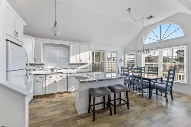 a kitchen with stainless steel appliances granite countertop a table chairs wooden floors a stove and white cabinets