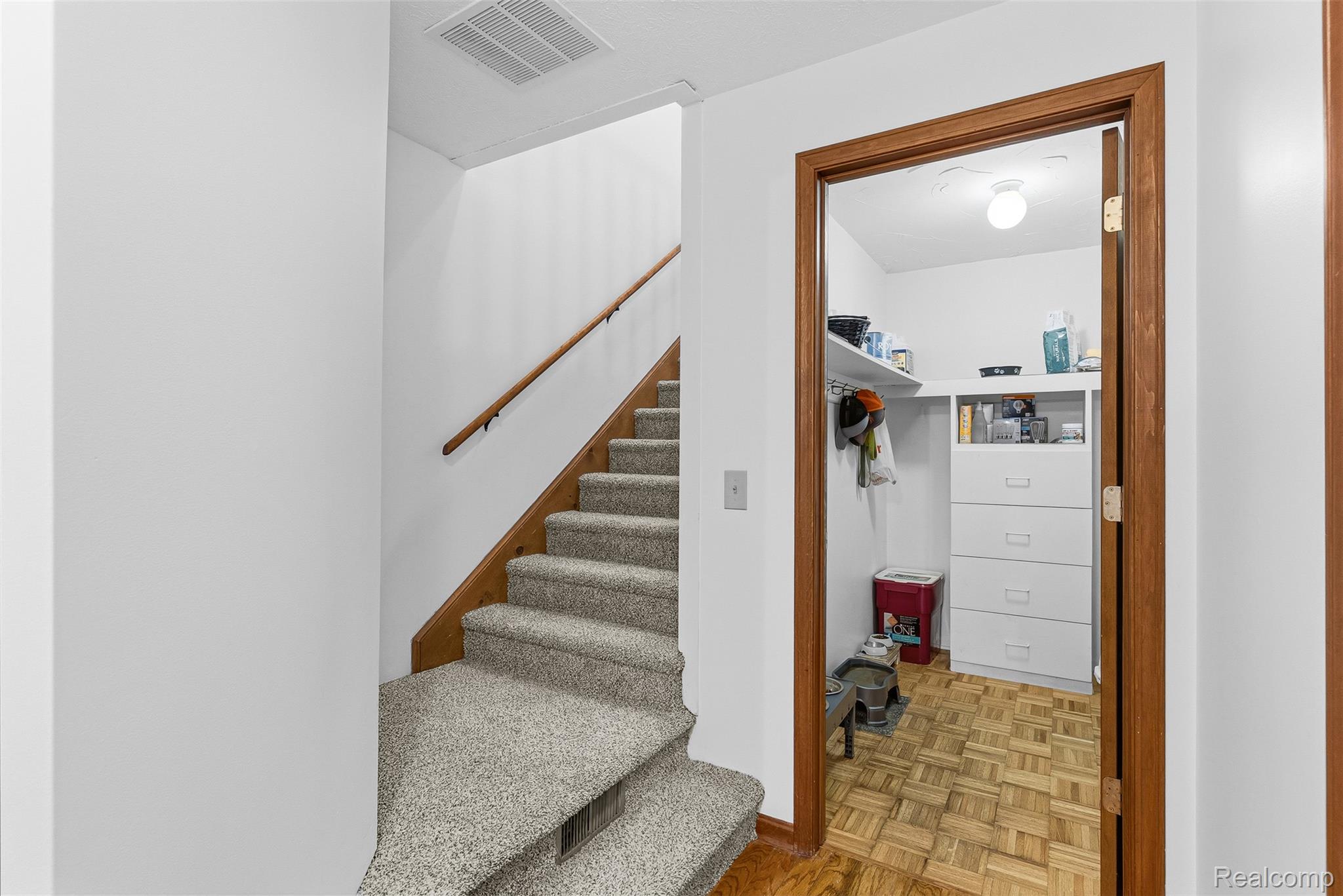 6699 Lansing Road Durand, MI 48429 - Photo 26 of 53 Carpeted staircase with a wood-finish handrail and base, featuring a doorway opening to a room with wood-finish parquet flooring and built-in shelving