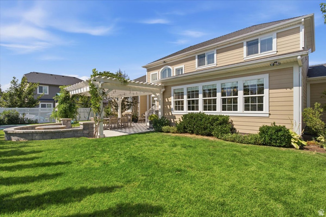 1257 Rigby Road Kaysville, UT 84037 - Photo 46 of 55 Expansive green lawn featuring a stone-faced fire pit with capstone accents, a spacious pergola-covered patio with checkered paving, and a tan-sided exterior with multiple white-framed windows