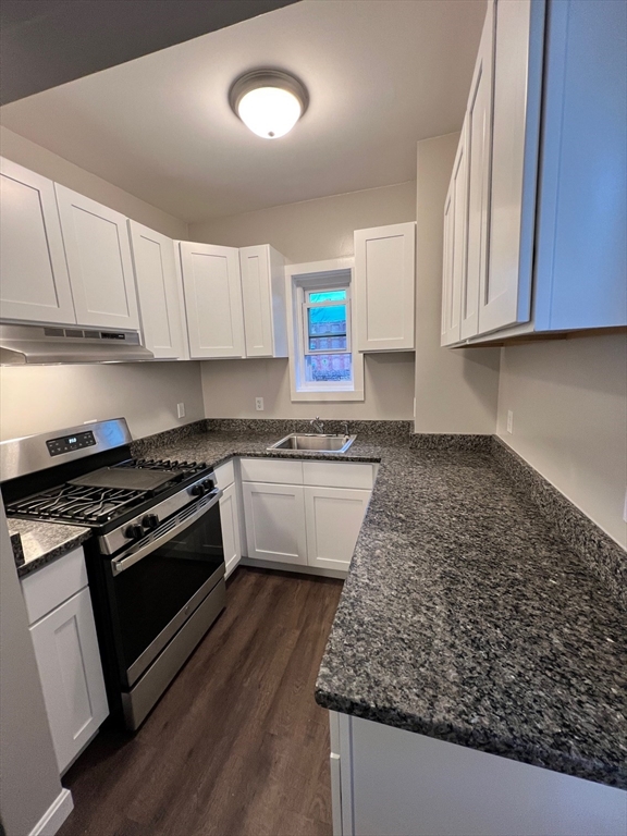 a kitchen with granite countertop a stove and a white cabinets
