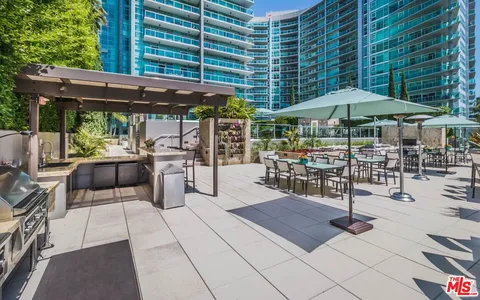 a view of a patio with a table and chairs under an umbrella with a barbeque