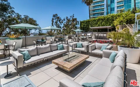 a view of a patio with couches table and chairs under an umbrella with a barbeque