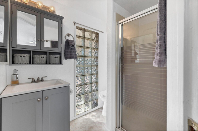 2990 East Riverside Drive, Unit 173 St. George, UT 84790 - Photo 16 of 38 Bathroom featuring a gray vanity with an integrated sink, a matching medicine cabinet, glass block window, and a glass-enclosed shower