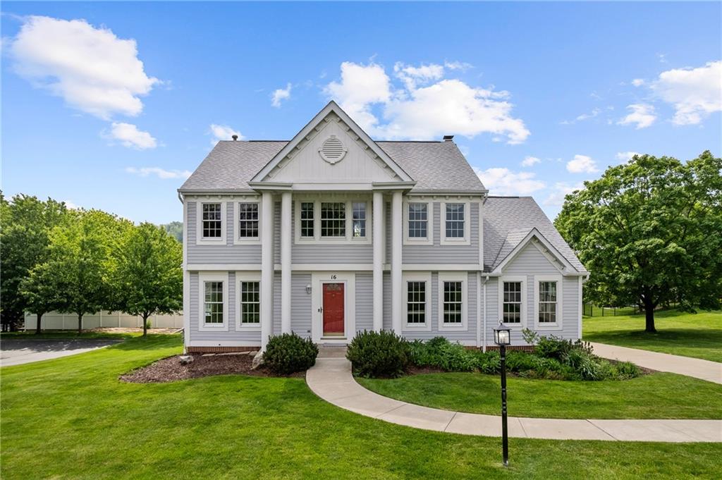 Charming Colonial-style home with timeless curb appeal, featuring a covered front porch with stately columns, a bold red door, and beautifully landscaped grounds