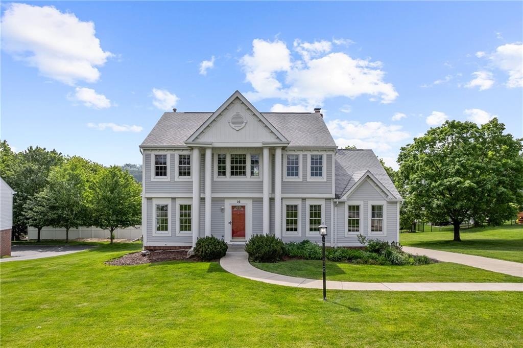 Charming Colonial-style home with timeless curb appeal, featuring a covered front porch with stately columns, a bold red door, and beautifully landscaped grounds