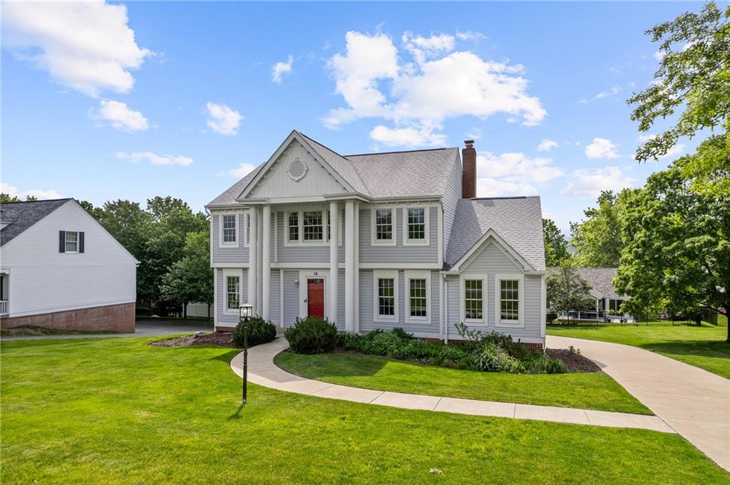 Charming Colonial-style home with timeless curb appeal, featuring a covered front porch with stately columns, a bold red door, and beautifully landscaped grounds
