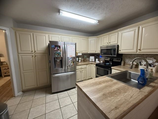 395 Austin Street Savannah, TN 38372 - Photo 5 of 32 Kitchen featuring extensive cream cabinetry, wood-finish countertops, stainless steel appliances, and diagonal tile flooring