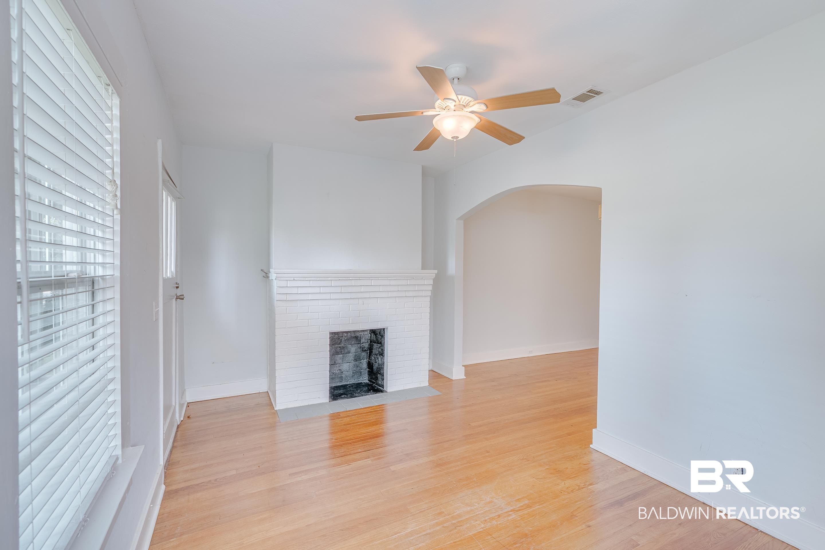 1852 Old Shell Road Mobile, AL 36607 - Photo 5 of 26 Unfurnished living room featuring arched walkways, ceiling fan, a fireplace, and light wood-style flooring