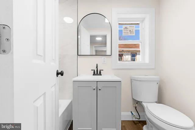 a bathroom with a toilet a sink a mirror and a window