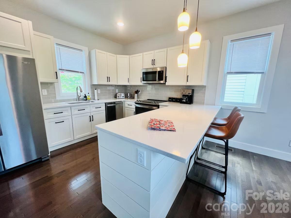 1063 Riverside Drive Asheville, NC 28804 - Photo 5 of 40 a kitchen with a refrigerator a stove top oven a sink dishwasher and white cabinets with wooden floor