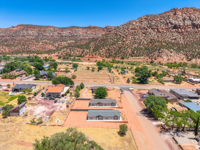464 Jessop Avenue Hildale, UT 84784 - Photo 53 of 73 Aerial perspective featuring two light-colored residences with dark roofs, set against a backdrop of natural red rock formations and scattered greenery