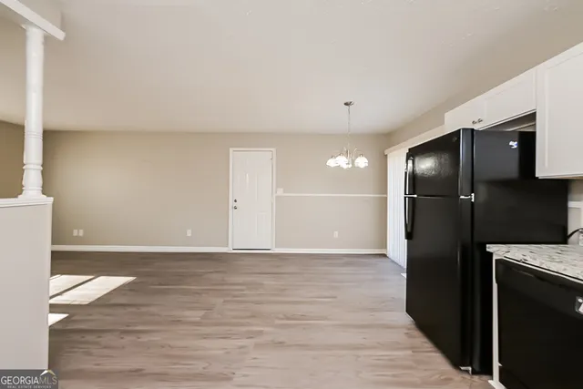a view of a refrigerator in kitchen and an empty room with wooden floor