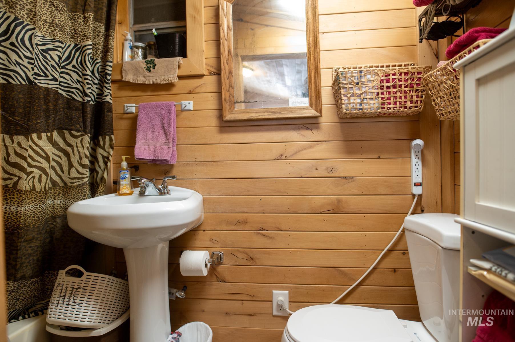 736 East Main Street Weiser, ID 83672 - Photo 23 of 33 Bathroom featuring horizontal wood paneling, a white pedestal sink with chrome fixtures, a white toilet, and a framed mirror