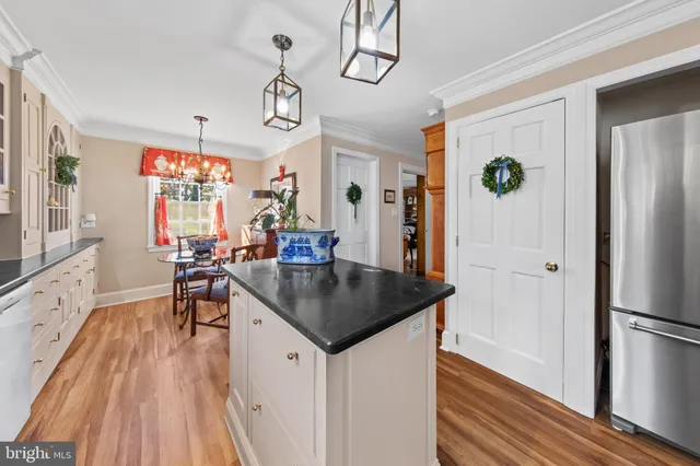 a kitchen with stainless steel appliances granite countertop a refrigerator a sink dishwasher a dining table and chairs with wooden floor