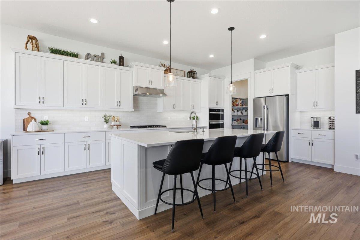 5512 North Ebony Way Meridian, ID 83646 - Photo 11 of 40 Kitchen with white cabinetry, a breakfast bar, stainless steel appliances, a kitchen island with sink, and dark wood-type flooring