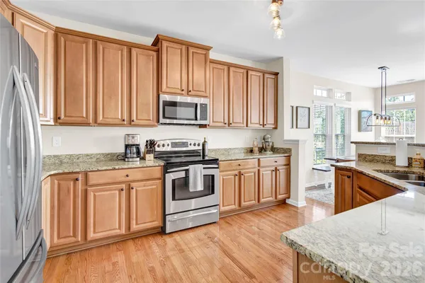 a kitchen with stainless steel appliances granite countertop a stove top oven a sink dishwasher and a refrigerator with wooden floor