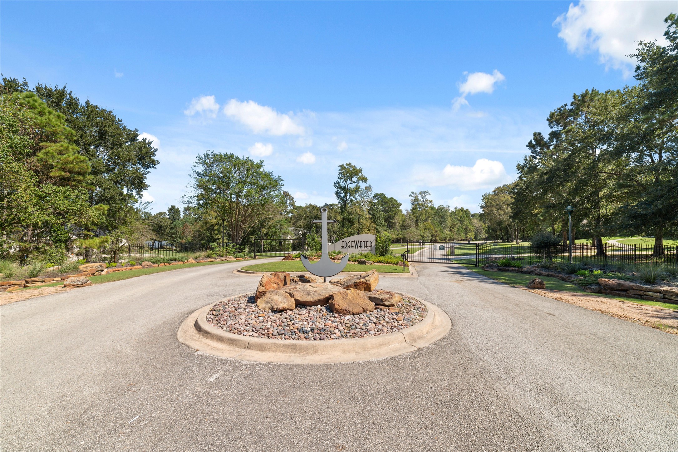 0 Ridgelake Court Montgomery, TX 77316 - Photo 19 of 29 Charming gated entrance to Edgewater, featuring a beautifully landscaped roundabout with natural stone accents, surrounded by lush greenery and mature trees.