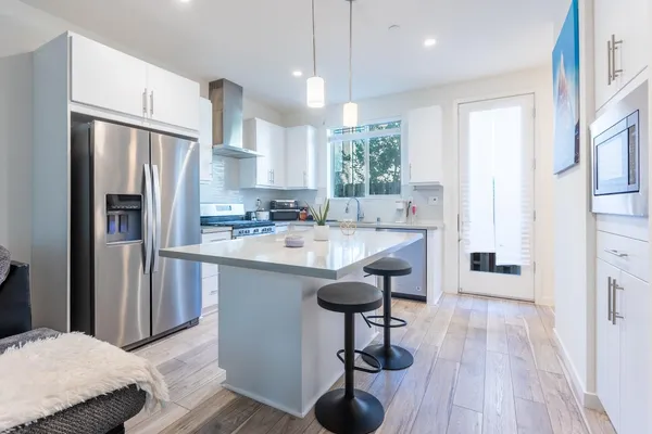 a kitchen with stainless steel appliances granite countertop a refrigerator a sink dishwasher a stove and white cabinets with wooden floor