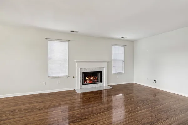 a view of an empty room with wooden floor fireplace and a window