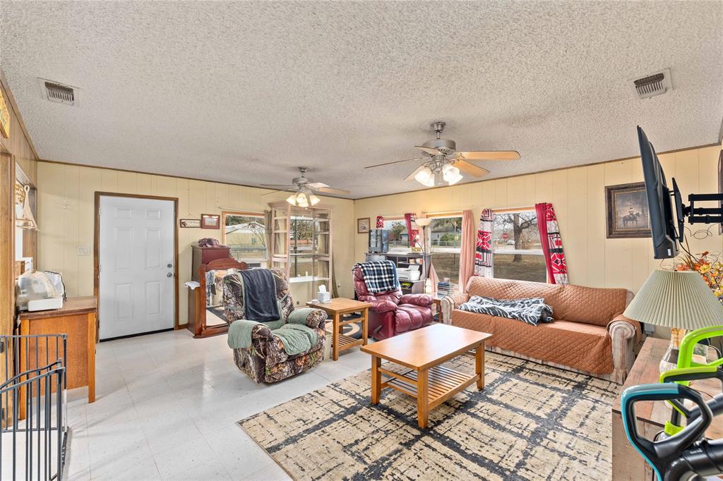 309 Goodwin Street Bangs, TX 76823 - Photo 6 of 20 Living area with tile patterned floors, wooden walls, ceiling fan, and a textured ceiling