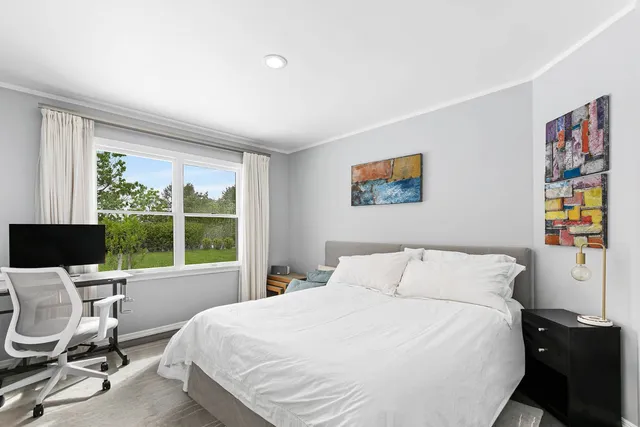 a bedroom with a bed a computer on the desk and a large window