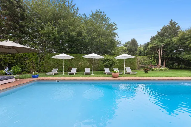a view of a swimming pool and lounge chairs in patio with a table and chairs under an umbrella
