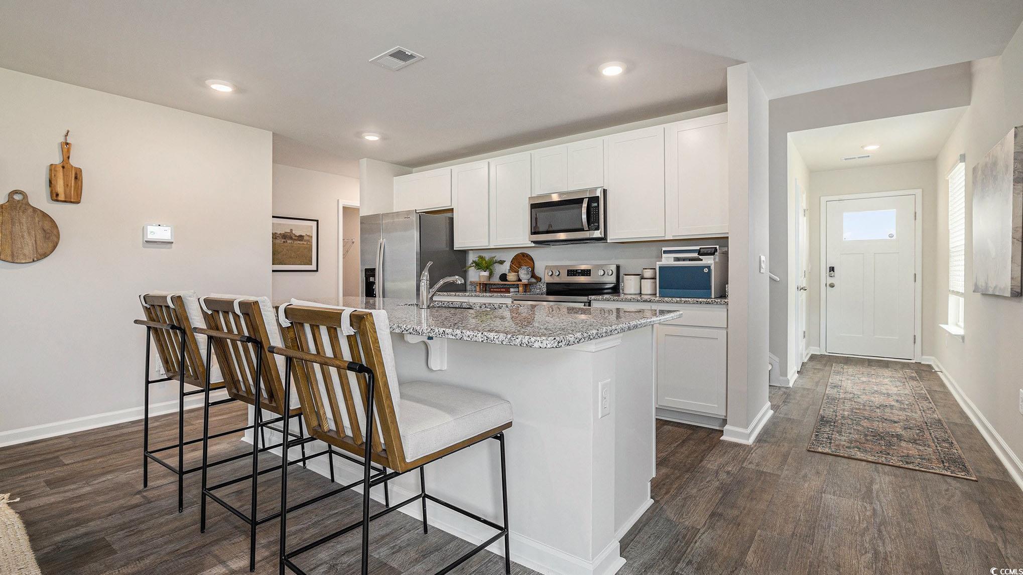 344 Skyward Street Myrtle Beach, SC 29588 - Photo 9 of 22 Kitchen featuring light stone counters, white cabinetry, appliances with stainless steel finishes, a breakfast bar area, and dark wood-style flooring